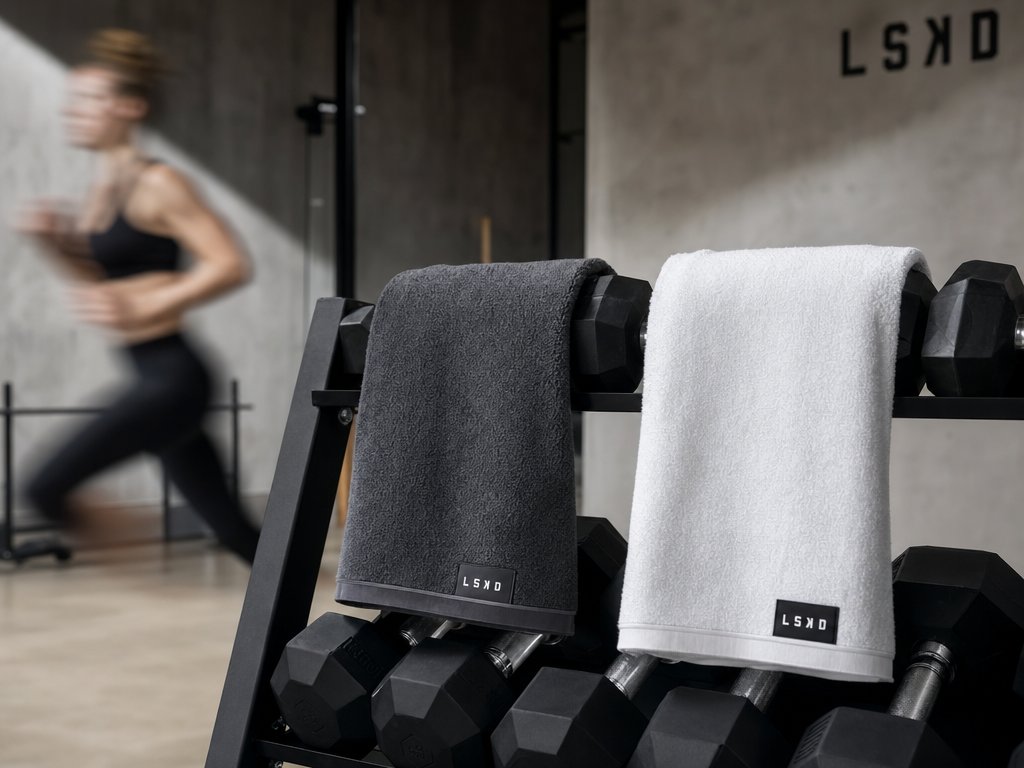 Charcoal and white gym towels with embroidered brand label on dumbbell rack